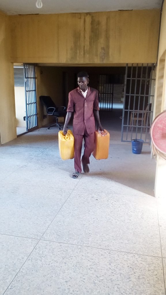 A cleaner carrying two jerry-cans to supply water to toilet on first floor of Office of Accountant-General, Ogun state secretariat